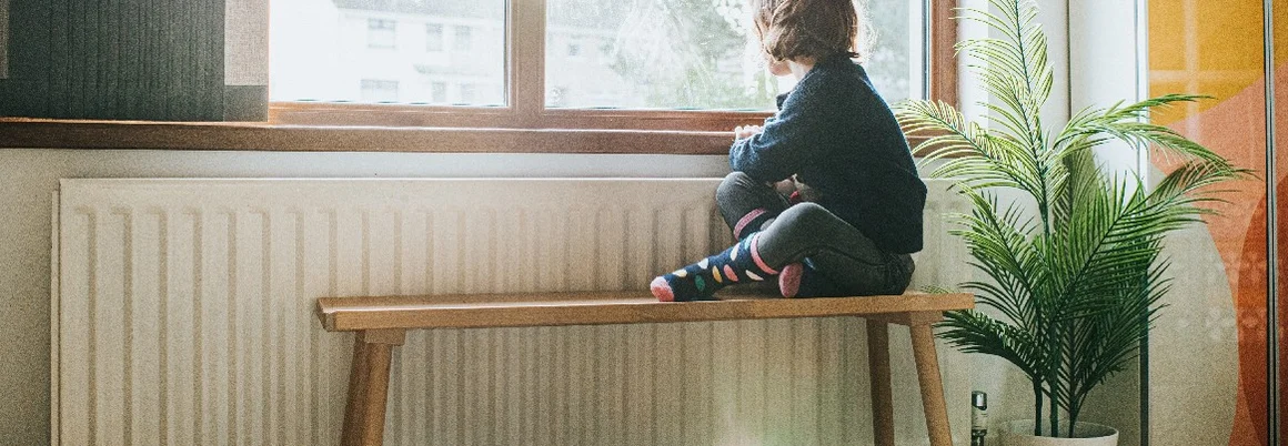 Kind sitzt auf Bank und schaut aus Fenster